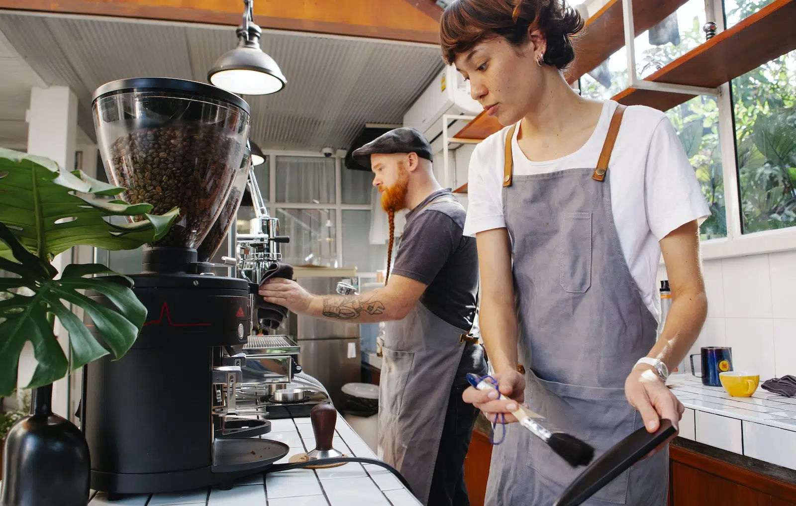Crop baristas against coffee maker and grinder in cafe kitchen
